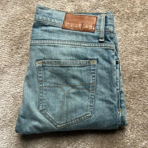  Jeans från Tiger of Sweden - Snygga ljusblå jeans från Tiger of Sweden med klassisk femficksdesign och slitning vid knät. Jeansen har raka ben och normal passform, tillverkade i mjukt bomullsjeansmaterial. Storleken är W29 och L32. Priset kan diskuteras.