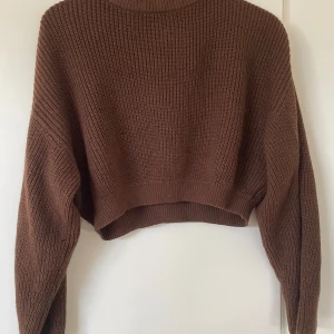 Brun croppad stickad tröja Divided - Säljer en brun croppad stickad tröja från Divided. Tröjan har lång ärm, ribbade muddar och en avslappnad passform. Perfekt för lager-på-lager under hösten eller vintern. Superenkel att styla med jeans eller kjol.