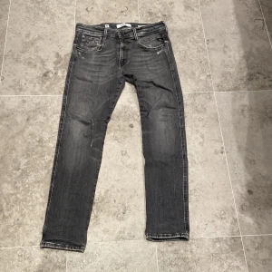 Replay Anbass grå slim jeans - Säljer ett par Replay Anbass jeans i grå tvätt med snyggt slitna detaljer. Jeansen hat en slim passform. Materialet är mjukt och stretchigt jeans. Blivit en defekt på höger knä men inget märk värdigt när den väl är på. Storlek 32,30, pris kan ändras vid köp!