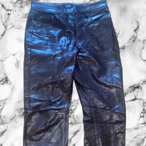Vinröda byxor med ormmönster - Säljer ett par blå metallic byxor från MAN med glansig finish och ormmönstrad struktur. Byxorna har klassisk femficksdesign och raka ben. Perfekta för dig som vill sticka ut med en unik look.