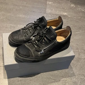 Svarta glitter sneakers från Giuseppe Zanotti - Säljer ett par svarta glitter sneakers från Giuseppe Zanotti med coola dragkedjor på sidorna och snörning framtill.