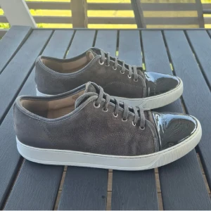 Lanvin - Snygga grå sneakers från Lanvin i mocka med vit sula och unika lackade tår i svart. Skorna har snörning och en klassisk låg profil som passar till det mesta. Perfekt för dig som vill ha något stilrent men ändå sticker ut med detaljer. Bra skick inga defekter. Storlek 8 motsvarar 42 men passar 43 