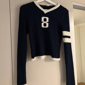 Mörkblå ribbad stickad tröja - Mörkblå stickad tröja med långa ärmar med vita ränder på ena ärmen och ribbade muddar vid hals, ärmslut och nederkant. Jätte söt lite high school aktig tröja!