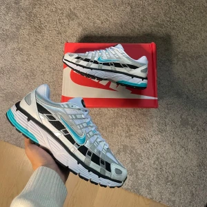 Nike p-6000 dusty cactus  - Nike sneakers med vit mesh, silver- och gråa detaljer samt svarta och turkosa inslag. Skorna har snörning, svart och vit sula med turkosa accenter och en klassisk Nike Swoosh i turkos på sidan. Perfekta för dig som gillar sportig och fräsch stil. Storlek 42, helt nya 