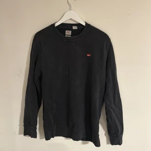 Svart sweatshirt från Levi's - Svart sweatshirt från Levi's med klassisk rund hals och liten röd logotyp på bröstet. Tröjan är i mjuk bomull, har långa ärmar och ribbade muddar vid ärmslut och nederkant. Perfekt för en chill och stilren look. Storleken är S men funkar även till M. Skriv vid minsta fundering🍾🌠