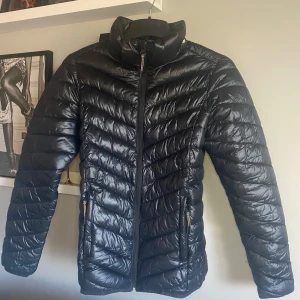 Svart pufferjacka från McKinley - Säljer en svart pufferjacka från McKinley i storlek 158/164. Jackan har snygga diagonala quiltade sömmar, hög krage och dragkedja framtill. Reflekterande detaljer baktill och två fickor med dragkedja. Perfekt för kalla dagar och riktigt chill stil.
