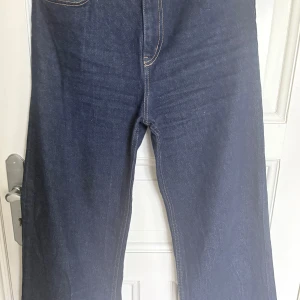 Mörkblå jeans från H&M, strl 40 - Mörkblå jeans från H&M i klassisk rak modell med kontrastsömmar. Byxorna har normal passform och raka ben, tillverkade i jeansmaterial. Perfekta för dig som gillar en enkel och stilren look.