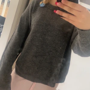 Mörkgrå stickad tröja - Mysig mörkgrå stickad tröja med rund halsringning och långa ärmar. Tröjan har en enkel och clean design med ribbade muddar vid ärmslut och nederkant. Perfekt för lager-på-lager under kyliga dagar.