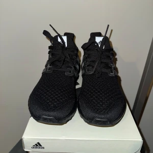 Adidas Ultraboost 1.0 W - Säljer ett par helsvarta Adidas Ultraboost sneakers med stickad ovandel och klassiska tre ränder på sidan. Skorna har snörning, platt sula och en bekväm boost-mellansula. Perfekta för dig som vill ha en stilren och sportig look. Aldrig använda.