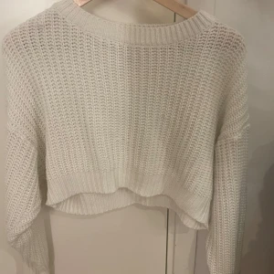 Vit croppad stickad tröja - Säljer en vit croppad stickad tröja med grovstickat mönster och rund halsringning. Tröjan har långa ärmar och ribbade muddar vid ärmslut och nederkant. Perfekt för lager-på-lager och chill stil.