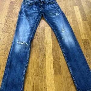 Blå slitna Crocker jeans skinny fit - Säljer ett par blå skinny jeans från Crocker med slitningar och hål på benen för en cool, avslappnad look. Jeansen har klassisk femficksmodell, dragkedja och läderpatch bak i midjan. Perfekta för dig som gillar streetstyle.