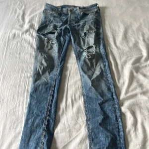 Jack and Jones 511 slitna blå jeans W28 L32 - Säljer ett par Jack and Jones 511 jeans i blå denim med slitningar och hål på låren för en riktigt avslappnad look. Klassisk femficksmodell med raka ben och normal passform. Perfekta för dig som gillar en streetig stil.