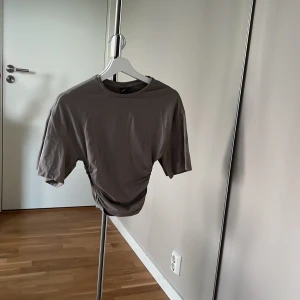 Grå/grön Tröja från Gina tricot  - Säljer en grå/grön topp  från Gina Tricot i storlek XXS. T-shirten har korta ärmar, rund halsringning och sitter åt i midjan . Perfekt för dig som gillar en enkel men trendig look. Inga tecken på användning 