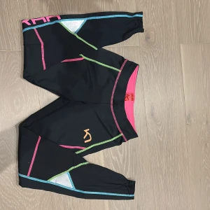 Svarta tränings sätt från Kari Traa  - Säljer ett par svarta träningstights och en tröja från Kari Traa i storlek XS. De har färgglada sömmar i rosa, blått och grönt samt detaljer i vitt. Tightsen har gummi vid ankeln för grepp och reflexer. De har dragkedjor vid anklarna och en där bak. Perfekt sett för dig som gillar sportig och färgstark stil. De funkar även bra som underställ.💕