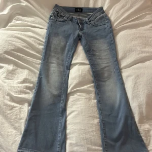 Ljusblå bootcut jeans  - Säljer ett par ljusblå bootcut jeans från ERA med snygga svarta broderier på bakfickorna. Jeansen har klassisk femficksdesign, låg midja och är tillverkade i mjukt denimtyg. Köpta på Plick men säljer då de inte passade mig, skriv för fler bilder eller funderingar 💕