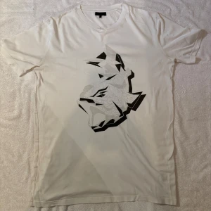 Vit Lanvin t shirt - Snygg vit t-shirt från Lanvin med ett unikt grafiskt tryck i svart och grått på framsidan. Klassisk passform med rund hals och korta ärmar. Tillverkad i mjuk bomull som känns skön mot huden. Perfekt för dig som gillar stilrena plagg med en twist.Storlek M, modellen är 179 65kg. Skriv vid minsta fråga, skickar snabbt🔥🔥🔥