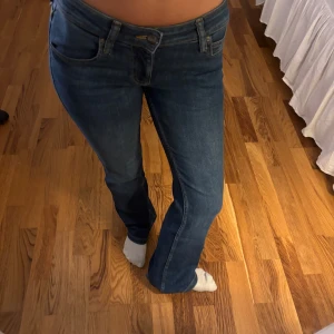Blå bootcut jeans med låg midja  från Lee - Säljer ett par klassiska blå jeans från Lee med bootcut passform. Jeansen har fem fickor, snygga kontrastsömmar och Lee-logga på bakfickan. Dem är low waist. 