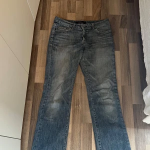 Blå bootcut jeans - Snygga blå jeans med bootcut passform. Jeansen har klassiska fem fickor, orange söm på bakfickorna. Håll som man ser på en av bilderna sen är dragkedjan sydd då den gick i sönder tyvärr. 