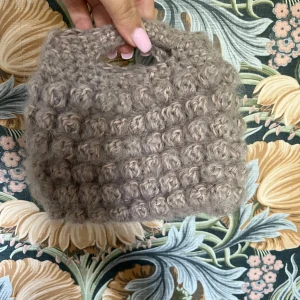 Beige stickad handväska med bubblig struktur - Superfin beige handväska i stickat material med bubblig struktur. Väskan har ett inbyggt handtag och är perfekt för dig som gillar unika accessoarer. Bredd 18cm, höjd 14cm💕skriv om du har frågor eller prisförslag 