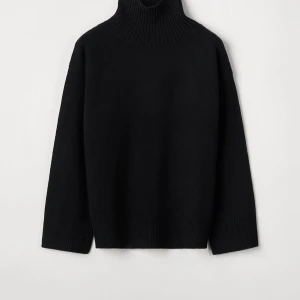 Svart polotröja i kashmir - Mysig svart polotröja med hög krage och avslappnad passform. Tröjan är stickad i mjuk kashmir och har breda ribbade muddar vid ärmslut och nederkant. Perfekt för lager-på-lager under kyliga dagar. Knappt använd från Soft Goat. 