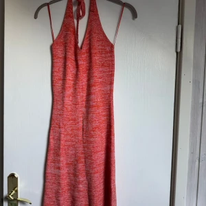 Korall halterneckklänning - Säljer en korallfärgad klänning med halterneck. Klänningen har en snygg v-ringning framtill och öppen rygg med knyt i nacken. Materialet är mjukt och stretchigt, perfekt för varma dagar. 