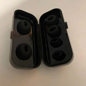Earbuds silikonproppar i förvaringsetui - Fyra par svarta silikonproppar för in-ear hörlurar i ett smidigt förvaringsetui. Passar de flesta trådlösa och kabelanslutna hörlurar. Propparna ser oanvända ut och etuiet är i gott skick med mindre ytliga repor 