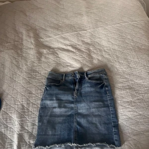 Jeanskjol från Pieces i XS - Snygg blå jeanskjol från Pieces i storlek XS. Kjolen är kort med rå kant nertill, klassiska fickor fram och bak samt hällor för bälte. Perfekt för dig som gillar en enkel men trendig denimlook.