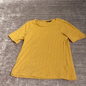 Gul ribbad t-shirt från LMTD - Gul t-shirt från LMTD i storlek XXS med ribbad struktur och korta ärmar. T-shirten har en rund halsringning och är gjord i mjuk bomull, perfekt för en chill och stilren look.