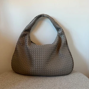 Axelväska design by si - Säljer en stor och mjuk grå axelväska från design by si Väskan är i fint skick och har flera innerfack. Perfekt för dig som gillar stilrena och trendiga accessoarer.