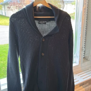 Mörkblå stickad kofta Brave Soul XS - Svart stickad kofta från Brave Soul i storlek XS. Koftan har grovstickad struktur, bred krage och knäpps med två stora knappar framtill. Långärmad och perfekt för lager-på-lager under kyliga dagar.