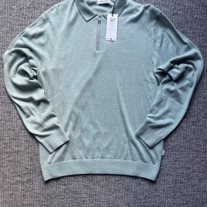 Grön halvzip pikétröja Jack & Jones - Snygg ljusgrön pikétröja från Jack & Jones med klassisk krage och halv dragkedja framtill. Tröjan är stickad i mjuk bomull och har långa ärmar med ribbade muddar. Perfekt för dig som gillar stilren och avslappnad look. Sitter som en stor S. Säljer för den är för stor för mig. Postar inom 1-2 dagar och svarar snabbt vid frågor😄