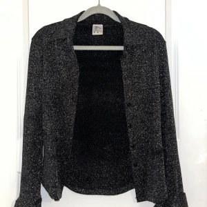 Svart glittrig skjorta från Authentic - Säljer en svart skjorta från Authentic med glittriga inslag. Skjortan har lång ärm, klassisk krage och knäppning framtill. Perfekt för dig som vill sticka ut lite extra med en snygg och glittrig look. Storlek M, S. Använd en gång. Köpt i Grekland. 