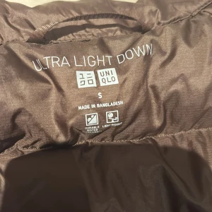 Brun dunväst från Uniqlo, storlek S - Säljer en brun, ultralätt dunväst från Uniqlo i storlek S. Västen har quiltad design, dragkedja framtill och är tillverkad i lätt och slitstarkt material. Perfekt för lager-på-lager och enkel att bära med sig. Snygg och smidig för dig som vill hålla stilen när det blir kyligt. ( ny pris 599kr ) Helt oanvänd 