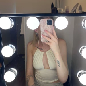 Krämvit halterneck topp med cut-out - Säljer en krämvit halterneck topp med snygg cut-out framtill. Toppen är ärmlös och har en tight passform som framhäver figuren. Perfekt för dig som gillar trendiga och stilrena plagg med en twist.