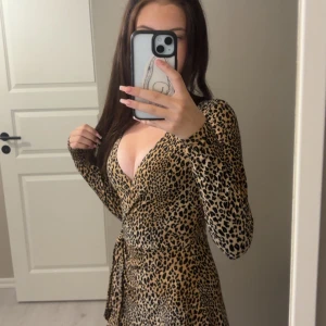 Leopardmönstrad omlottklänning - Säljer en snygg leopardmönstrad kort omlottklänning med lång ärm och djup v-ringning. Klänningen har knyt i midjan och är i ett mjukt, följsamt material. Perfekt för dig 