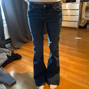Blå bootcut jeans med hög midja - Snygga blå jeans med bootcut-modell och låg midja. Klassisk femficksdesign och dragkedja med knapp framtill. Jeansen har en mörkblå tvätt och är tillverkade i ett robust jeanstyg som ger en tidlös look.