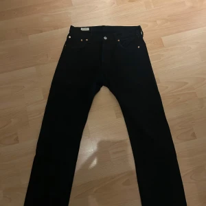Svarta Levi's 501 jeans W30 L32 - Klassiska svarta Levi's 501 jeans med raka ben och femficksmodell. Jeansen har knappgylf och detaljer i metall. Perfekta för dig som gillar en tidlös och clean look. Tillverkade i slitstarkt jeanstyg.