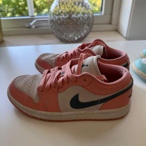 Nike Jordan 1 Low i rosa och beige - Säljer ett par Nike Jordan 1 Low med snygg färgkombo av rosa och beige mocka samt läder. Skorna har klassisk svart swoosh, rosa snörning och perforerad tå. Perfekta sneakers för dig som vill sticka ut med en unik färg på dina kicks. Nypris 5000kr från Dubai.