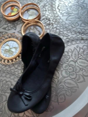 Fins oanvända Svarta ballerinaskor med rosett  - HEJSAN 👋 Säljes ett par Klassiska svarta ballerinaskor från DS Shoes by din sko i storlek 38. Skorna har rund tå, en söt rosettdetalj framtill och slät ovansida i syntetmaterial. Sulan är ljus med ingraverade blommor för extra stilpoäng. Bekvämt lätta och dra på.  Obs Inga fjärilar i bakgrunden ingår. Annonsen gäller endast för ett par skor.Kontakta mig gärna innan köp tack. Mvh Anna 