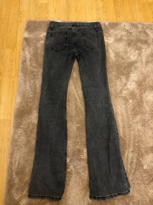 Svarta bootcut jeans - Säljer ett par svarta bootcut jeans med klassisk femficksdesign och slitning på ena benet. Jeansen har en snygg tvättad look och är tillverkade i mjukt denimtyg. Perfekta för dig som gillar en avslappnad men ändå trendig stil.
