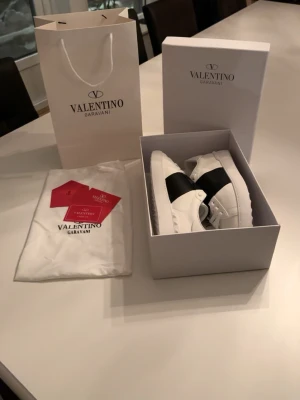 Valentino Garavani Open sneakers vit/svart - Säljer ett par Valentino Garavani Open sneakers i vitt skinn med bred svart rem över vristen. Klassisk rund tå, vita snören och cool räfflad sula. Kommer med originalkartong, dustbag och tags. Perfekta för dig som vill ha en clean men lyxig look.