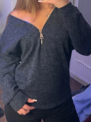 Mörkgrå tröja med dragkedja Creme Fraiche - Mysig mörkgrå tröja från Creme Fraiche med en stor silverfärgad dragkedja framtill. 