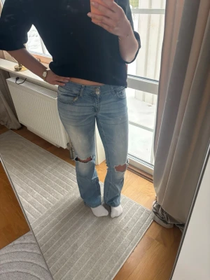 Ljusblå bootcut jeans med slitningar - Säljer ett par ljusblå jeans med bootcut passform och slitna hål över knäna. 