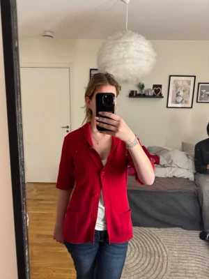 Stickad kofta - Number One - Säljer en supersnygg, djupröd stickad kofta från märket Number One. Koftan har en smickrande sjalkrage, dekorativa knappar och två praktiska fickor framtill. Den korta ärmen ger den en modern touch och gör den perfekt att bära över en blus eller ett linne. Ett tidlöst plagg i en fantastisk färg som lyfter vilken outfit som helst! • Märke: Number One. • Storlek: 44/46. • Detaljer: Sjalkrage, korta ärmar, fickor fram. • Skick: Mycket fint skick.