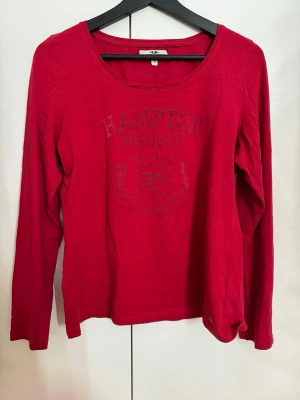 Röd långärmad topp Hampton Republic - Klassisk röd långärmad t-shirt från Hampton Republic. Toppen har ett snyggt, diskret tryck på bröstet med texten "Hampton Republic N.Y USA" och ett emblem. Mjuk och skön kvalitet med en rundad urringning. Perfekt till jeans för en sportig och fräsch vardagslook! • Märke: Hampton Republic. • Storlek: M. Men passar en S om man vill ha en lite större tröja:) • Detaljer: Tryck på bröstet, lång ärm. • Skick: Bra begagnat skick.