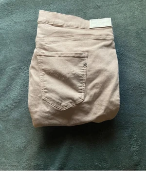 Beige Replay Anbass jeans slim fit - Säljer ett par snygga beige Replay Anbass jeans med klassisk femficksdesign och diskret logga på bakfickan. Jeansen har slim passform och är tillverkade i mjuk bomullsmix med lite stretch för extra komfort. Perfekta för en clean och stilren look.