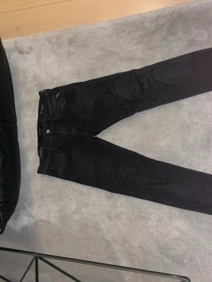 Svarta Replay Hyperflex jeans - Säljer ett par svarta Replay Hyperflex jeans i modell Anbass. De har en slim passform med klassisk femficksdesign och stretchigt material som gör dem riktigt sköna. Perfekta om du gillar jeans som sitter tajt men ändå är flexibla. Stängs med dragkedja och knapp.