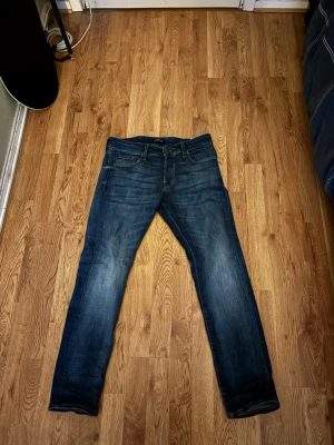 Blå jeans från Jack & Jones, 30/30 - Säljer ett par klassiska blå jeans från Jack & Jones i storlek 30/30. Jeansen har en snygg tvätt med lätt slitning, fem fickor och raka ben. Perfekta till vardags och passar till det mesta. Materialet är tåligt denim som håller länge.