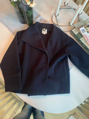 Marinblå kappa från Gina Tricot - Stilren svart kappa från Gina Tricot med bred krage och knappar framtill. Klassisk rak modell som är enkel att matcha till olika outfits. Perfekt för dig som gillar en clean och tidlös look. Nypris: 399 kr🤗