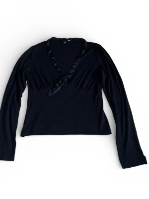 Svart långärmad topp med satinrosett - Svart långärmad topp från H&M med v-ringning och satinrosett framtill. Kragen är kantad med glansigt satinband. Toppen är i bra skick utan tecken på användning. Storlek m men upplever att den passar mer som en s/xs.